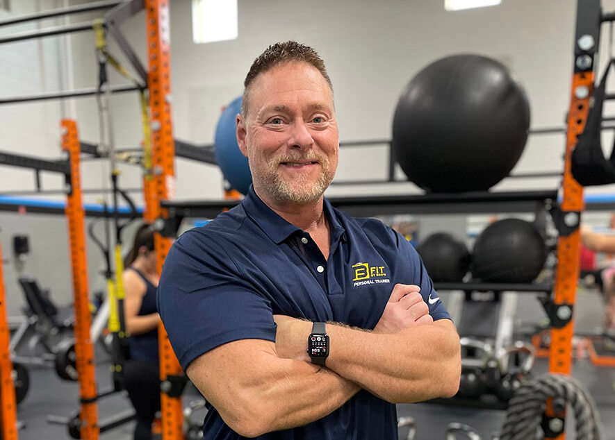 Personal trainer smiling in gym with equipment.