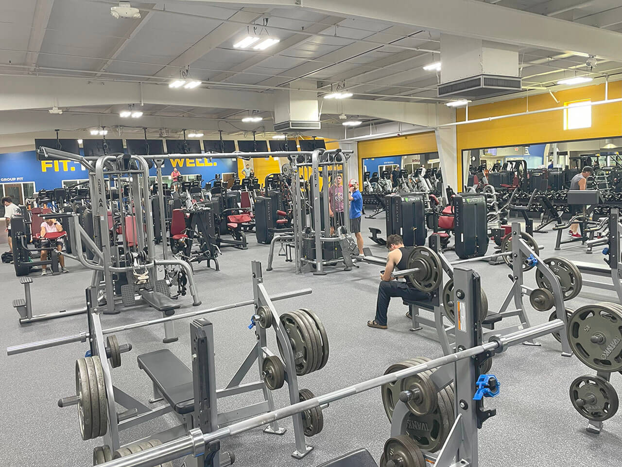 Spacious gym with various fitness equipment and people working out.