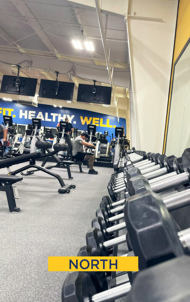 Gym with exercise machines and dumbbells, 'North' sign.